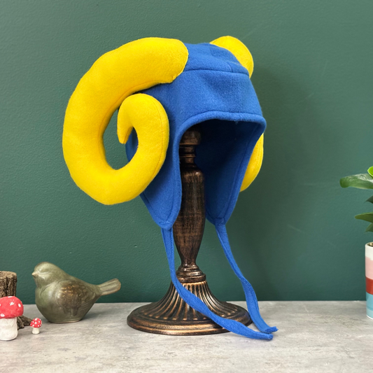 Blue and yellow ram hat on a stand with decorative items on a table against a green wall.