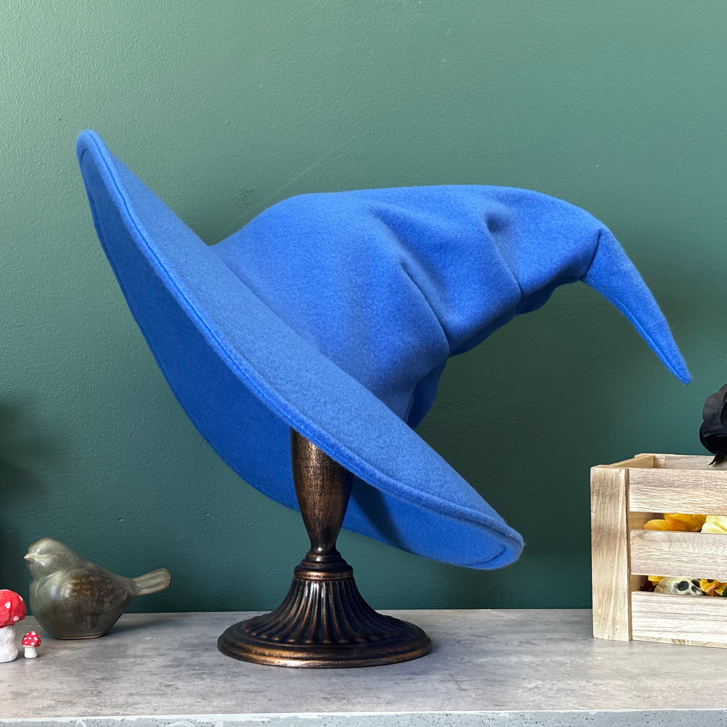 Blue witch hat on a stand against a green wall with decorative items around.