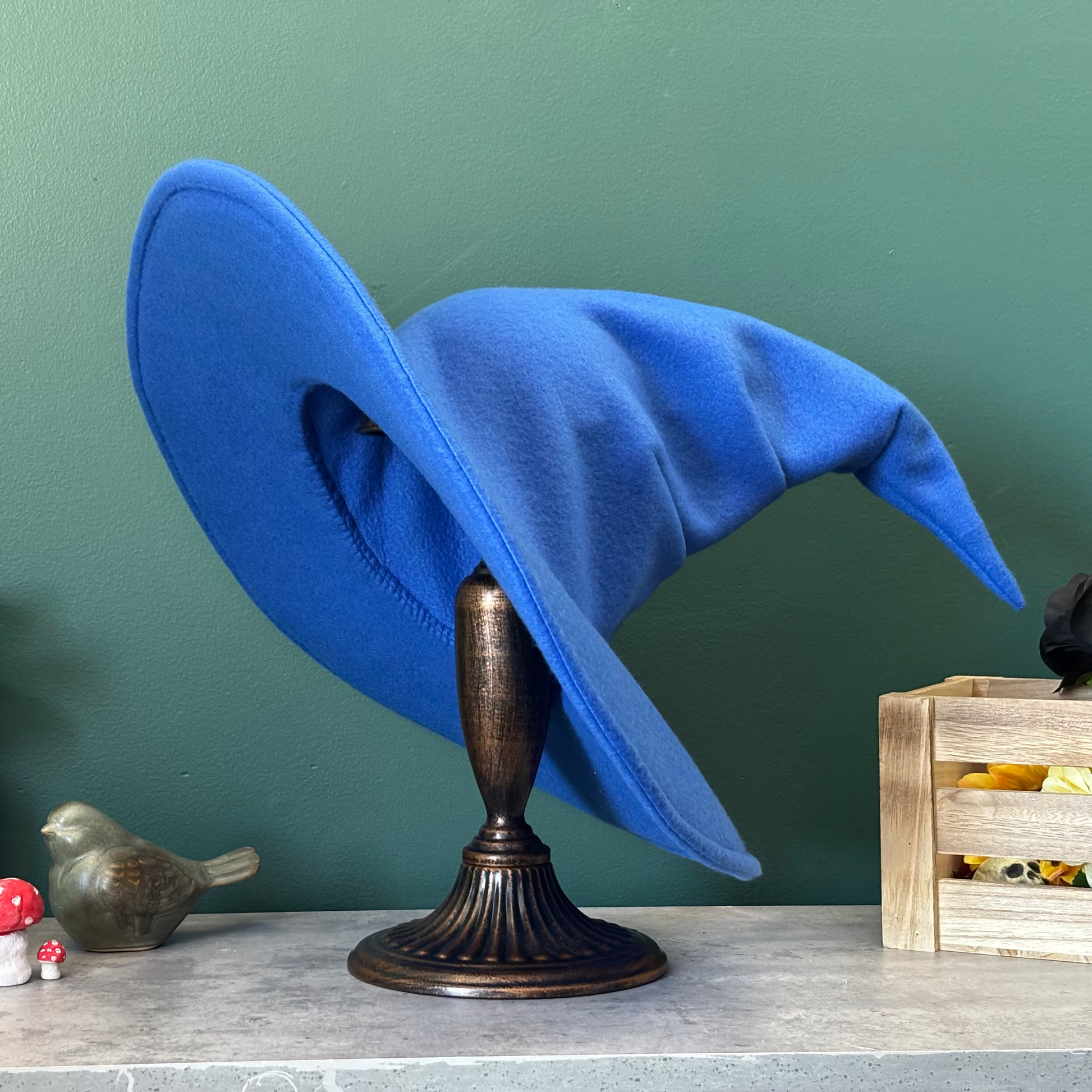 Blue witch hat on a stand against a green wall with decorative items around.
